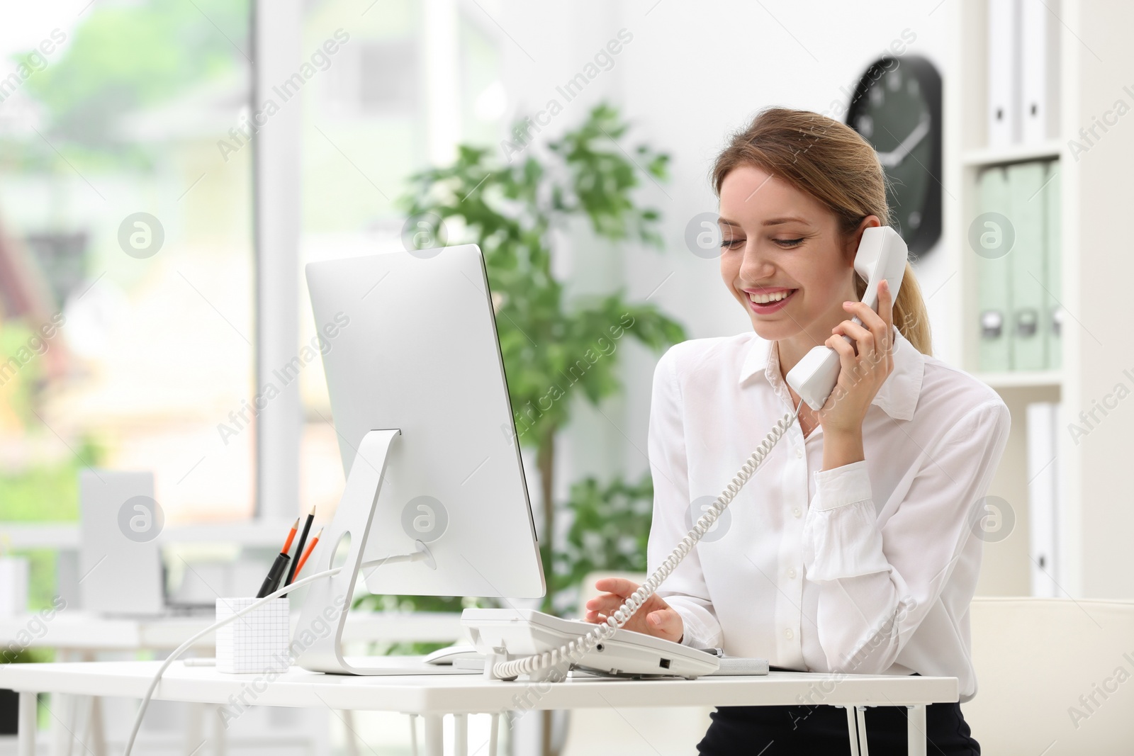 Photo of Female receptionist talking on phone at desk in office