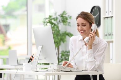 Photo of Female receptionist talking on phone at desk in office