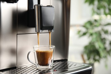 Espresso machine pouring coffee into glass cup against blurred background, closeup. Space for text