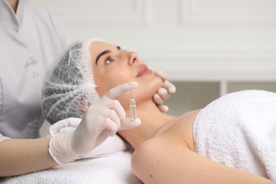 Professional cosmetologist holding skincare ampoule while working with client in clinic, closeup