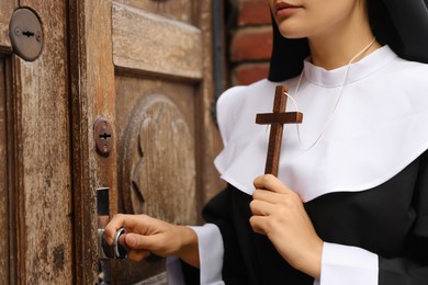 Young nun with Christian cross near wooden door, closeup