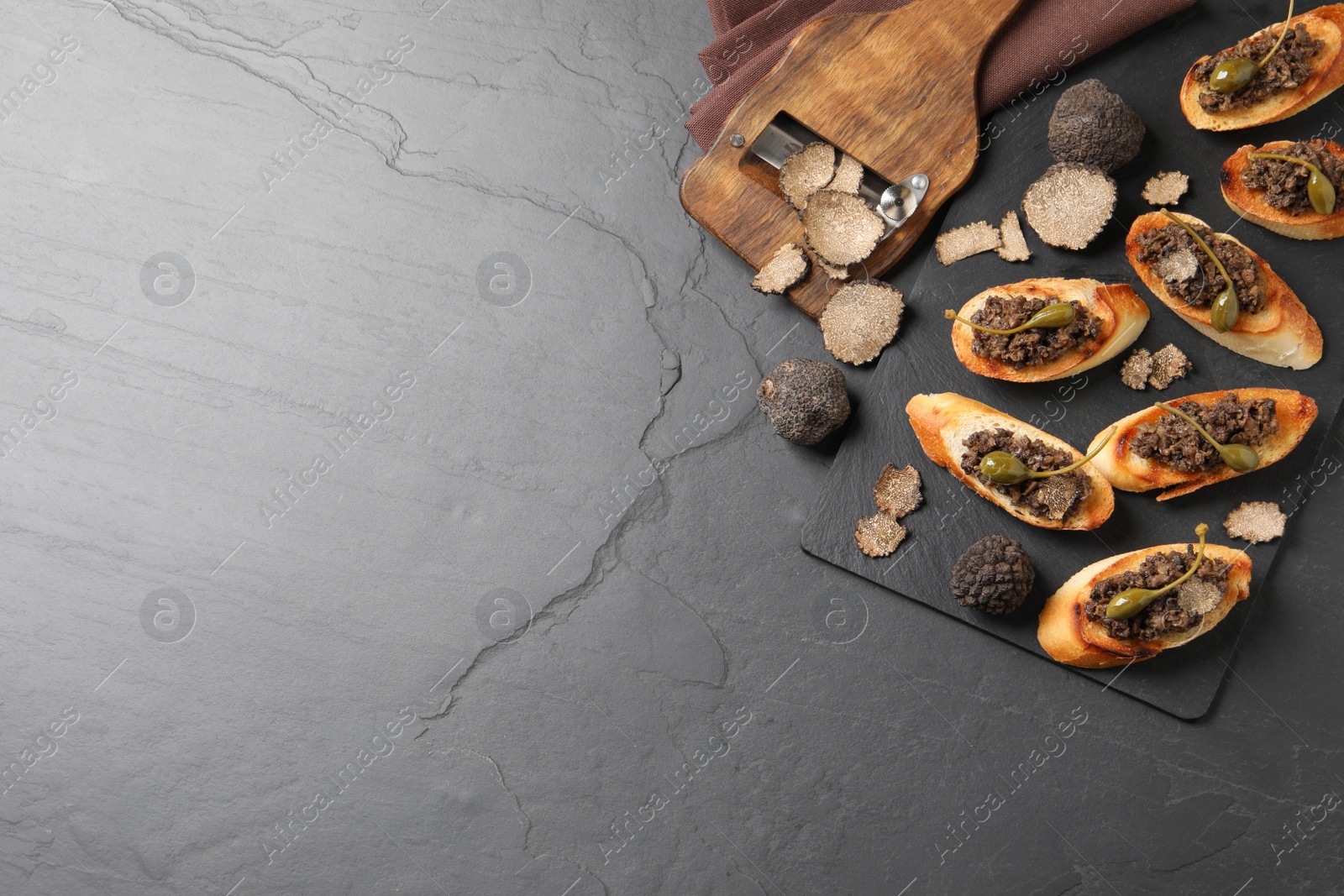 Photo of Tasty bruschettas with truffle paste and capers on black table, flat lay. Space for text