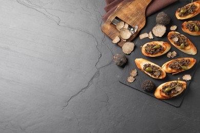 Photo of Tasty bruschettas with truffle paste and capers on black table, flat lay. Space for text