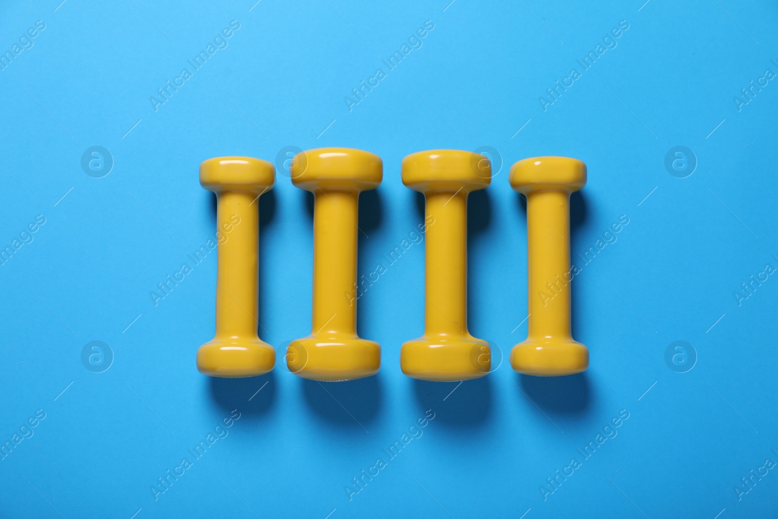 Photo of Yellow dumbbells on light blue background, flat lay. Morning exercise