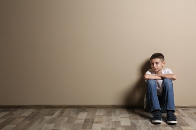 Upset boy sitting on floor at color wall. Space for text