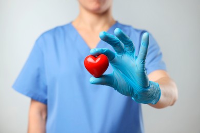 Photo of Doctor wearing light blue medical glove holding decorative heart on grey background, closeup