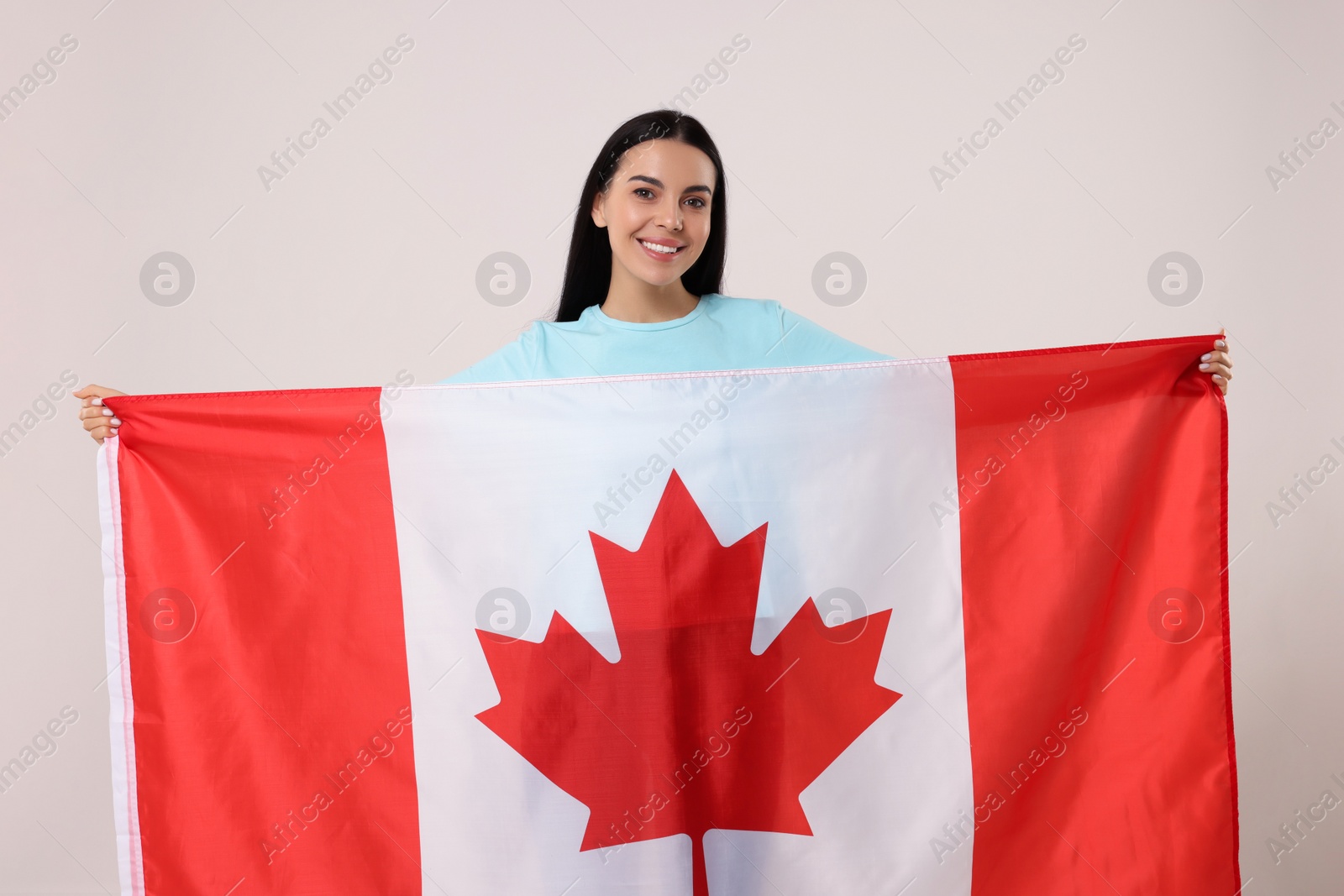 Photo of Happy young woman with flag of Canada on beige background