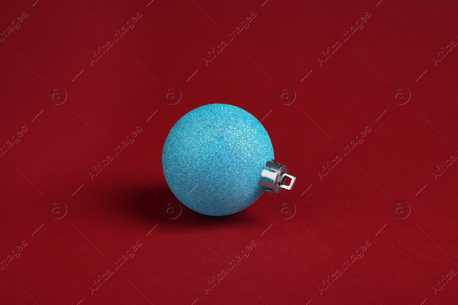 Photo of One light blue Christmas ball on red background