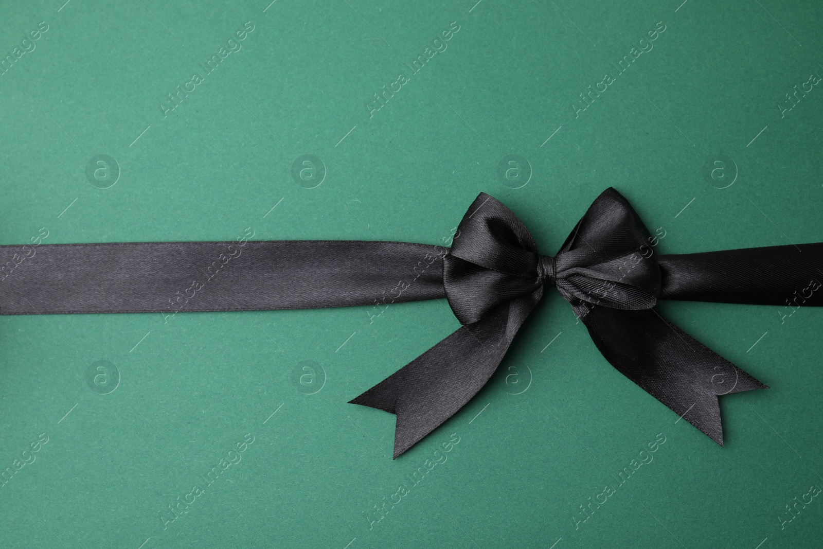 Photo of Black satin ribbon with bow on green background, top view