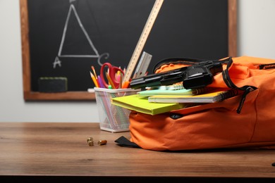 Photo of Gun, bullets and school stationery on wooden table near blackboard indoors