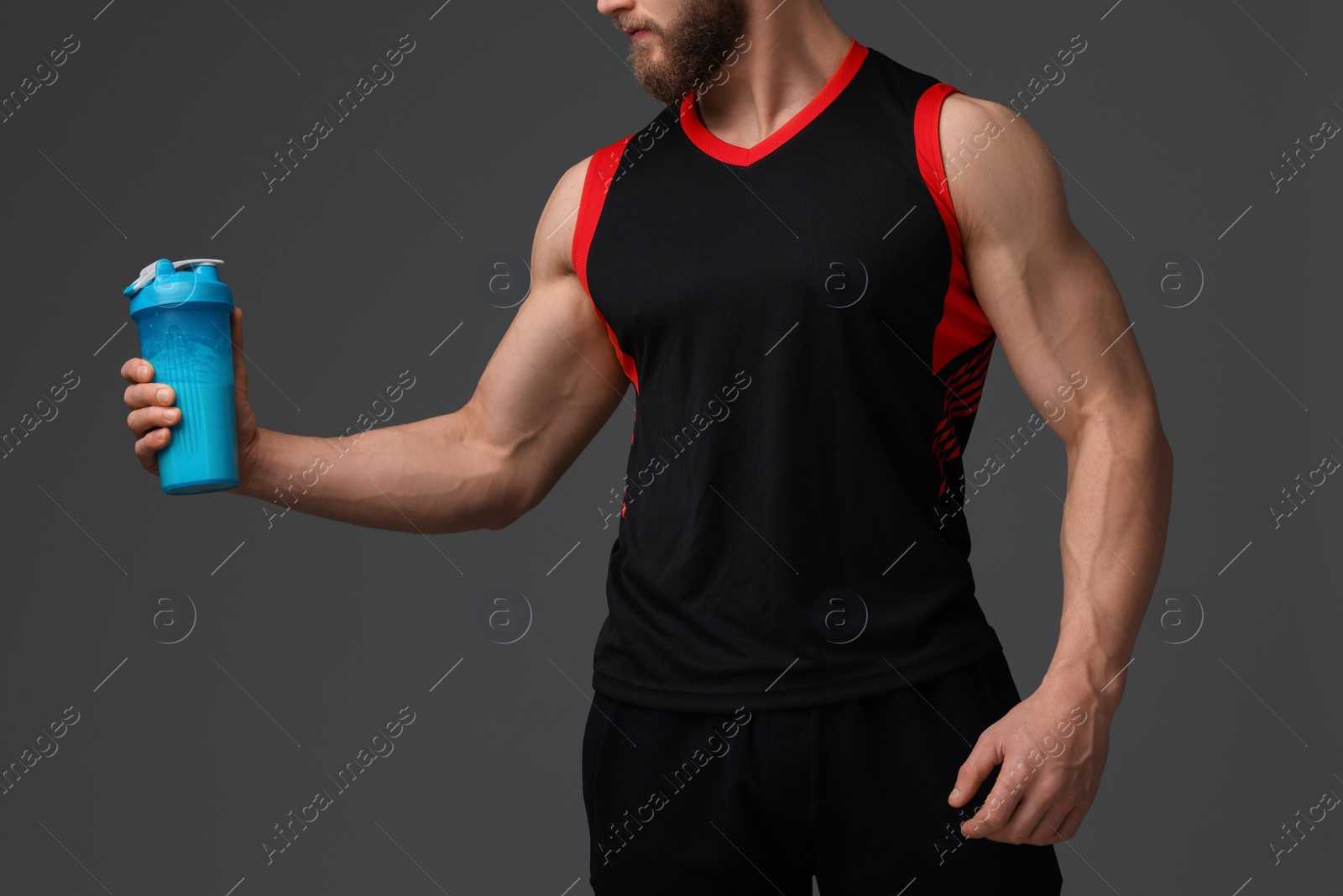 Photo of Young man with muscular body holding shaker of protein on grey background, closeup