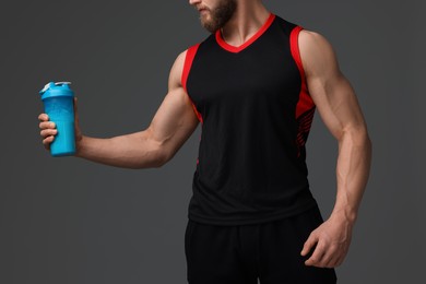 Young man with muscular body holding shaker of protein on grey background, closeup