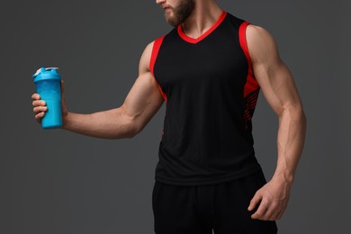 Photo of Young man with muscular body holding shaker of protein on grey background, closeup