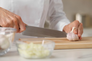 Photo of Professional chef cutting garlic at white marble table indoors, closeup