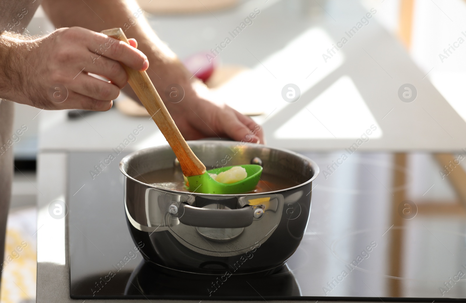 Photo of Young man cooking delicious soup in kitchen, closeup