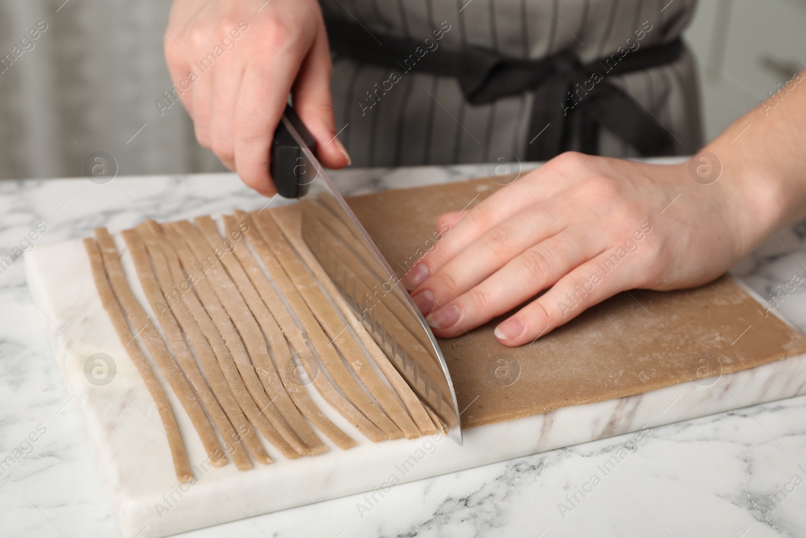 Photo of Woman making soba (buckwheat noodles) with knife at white marble table indoors, closeup