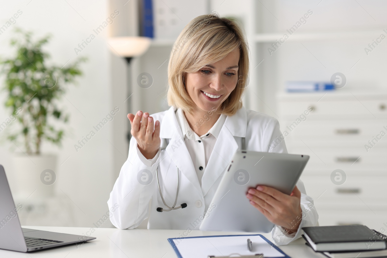 Photo of Smiling doctor with tablet having online consultation at table in office