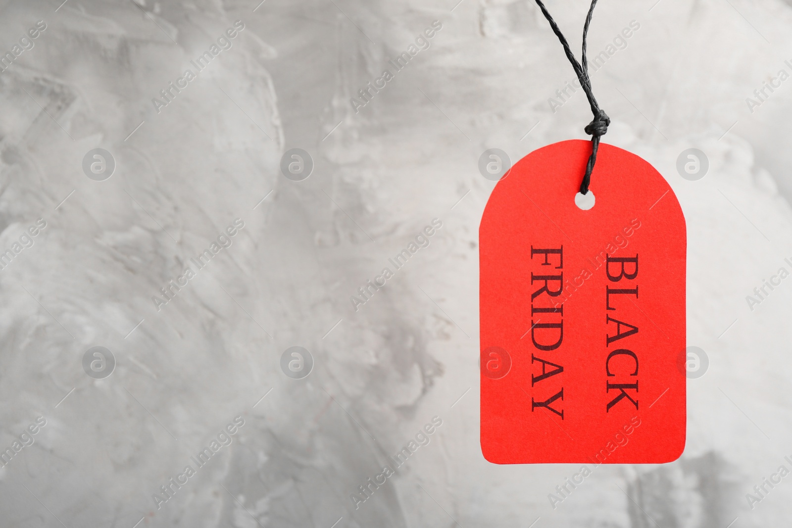 Photo of Red tag with words BLACK FRIDAY hanging on light grey background. Space for text
