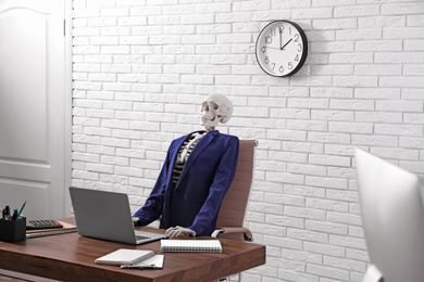 Photo of Human skeleton in suit using laptop at table in office