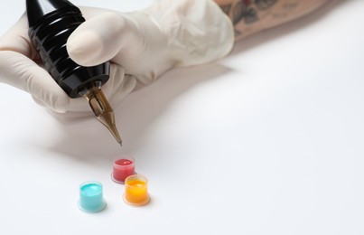 Photo of Tattoo artist with professional machine and colorful ink on white background, closeup