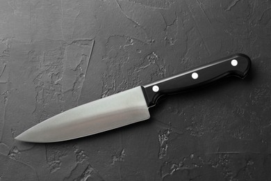 Photo of One sharp knife on dark textured table, top view