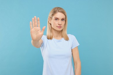 Photo of Woman showing stop gesture on light blue background