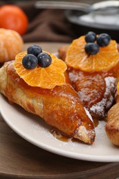 Photo of Fresh tasty puff pastry with sugar powder, jam, tangerines and blueberries on wooden table, closeup