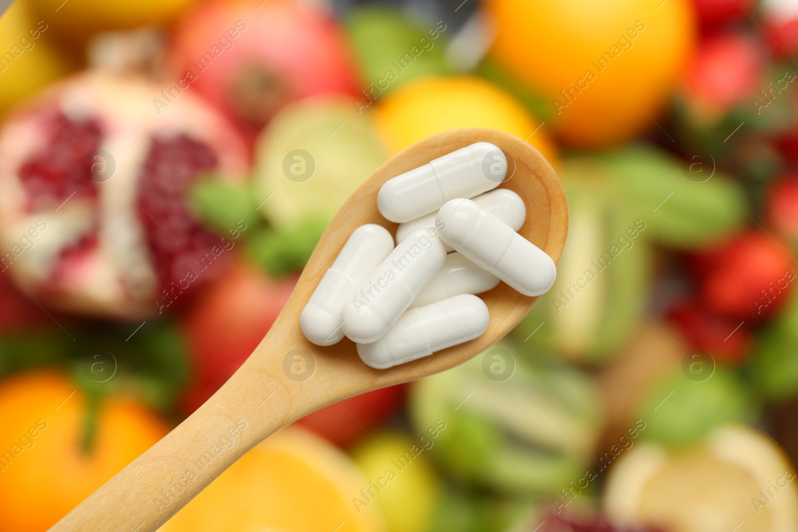 Photo of Vitamin pills in spoon over fresh fruits, top view