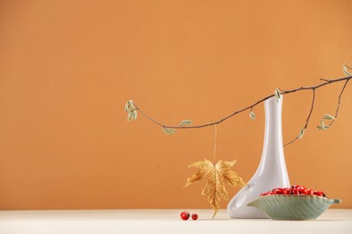 Photo of Composition with tree branch, autumn leaf and red berries on white table against orange background, space for text