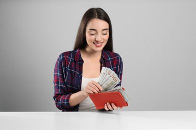 Young woman with money and wallet at table on light grey background