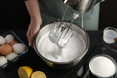 Photo of Woman making whipped cream with hand mixer at black table, closeup