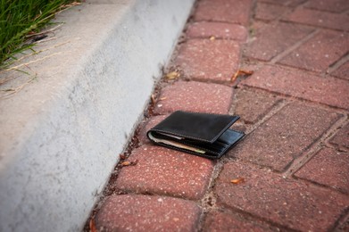 Photo of Black wallet on pavement outdoors. Lost and found