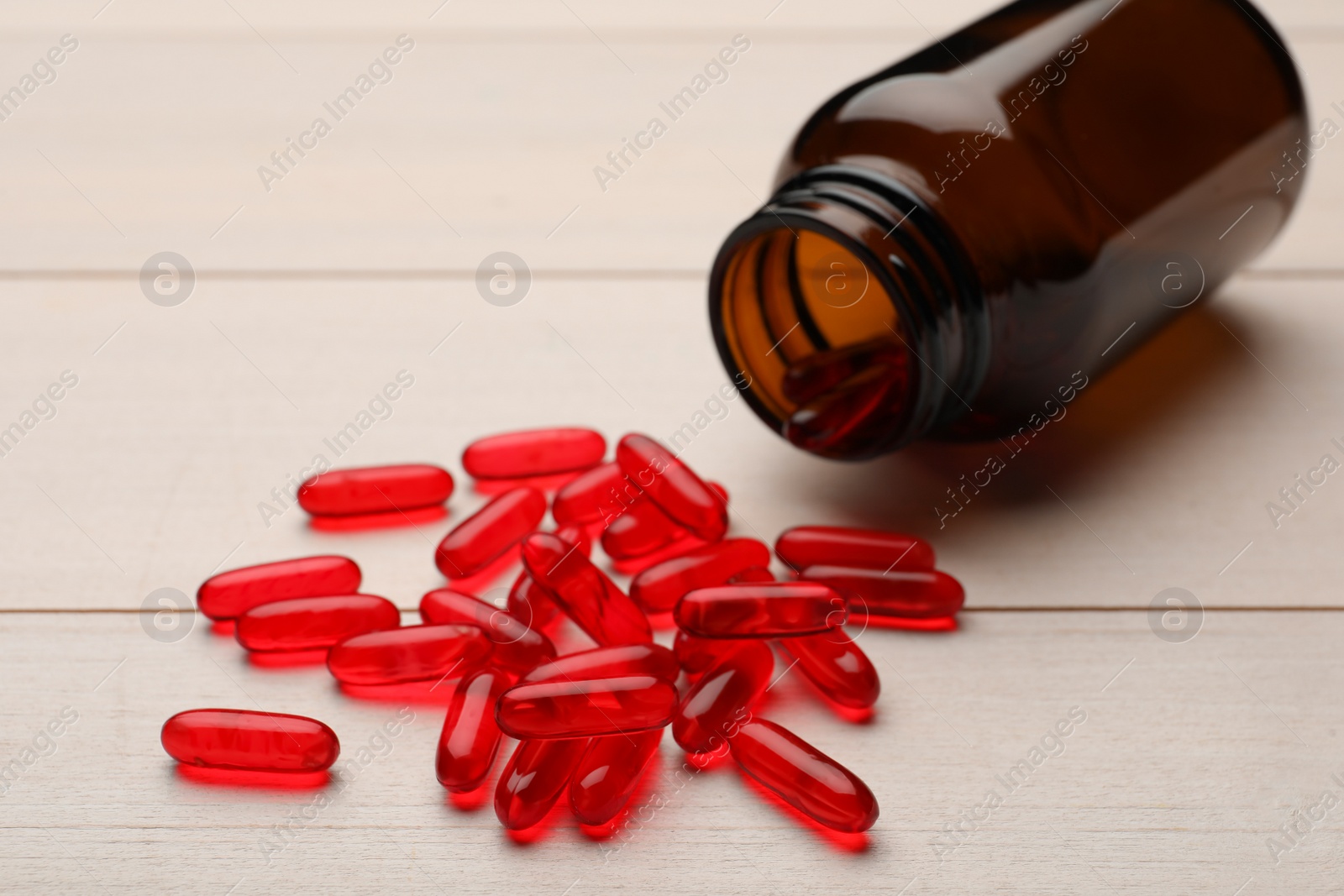 Photo of Overturned bottle with dietary supplement capsules on white wooden table, closeup