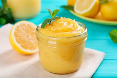 Photo of Delicious lemon curd in glass jar, fresh citrus fruit and mint on light blue wooden table, closeup