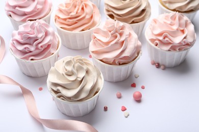 Photo of Many tasty cupcakes, sprinkles and ribbon on white background, closeup