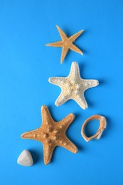 Photo of Beautiful starfishes and stone on blue background, flat lay
