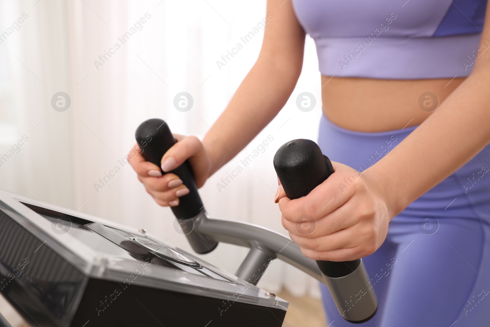 Photo of Woman using modern elliptical machine indoors, closeup