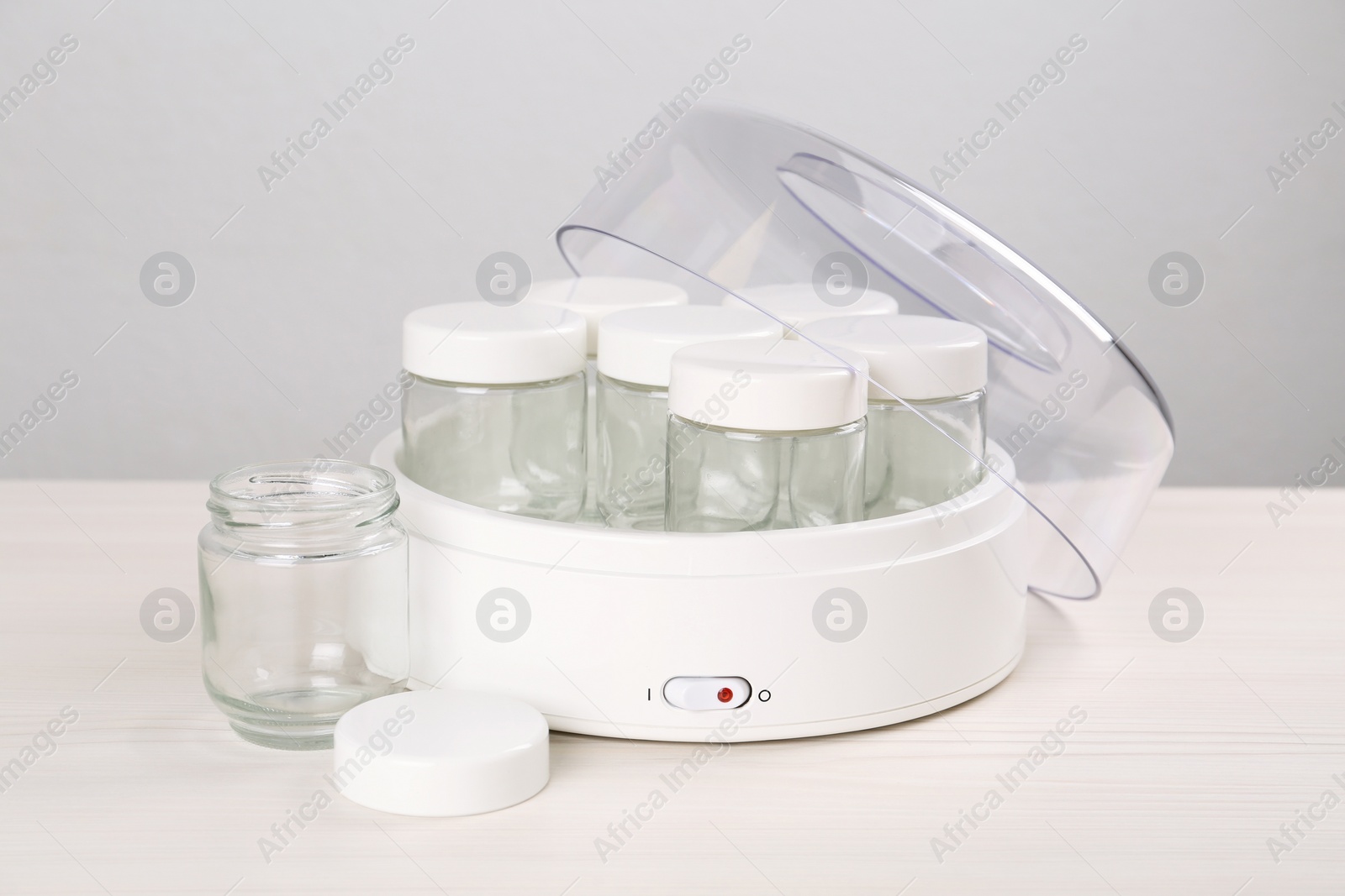 Photo of Modern yogurt maker with empty jars on white wooden table