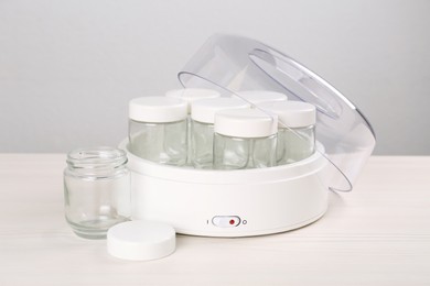 Photo of Modern yogurt maker with empty jars on white wooden table