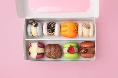 Cardboard box with delicious macarons on pink table, top view