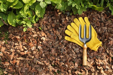 Photo of Soil mulched with bark chips, fork and gloves in garden, flat lay