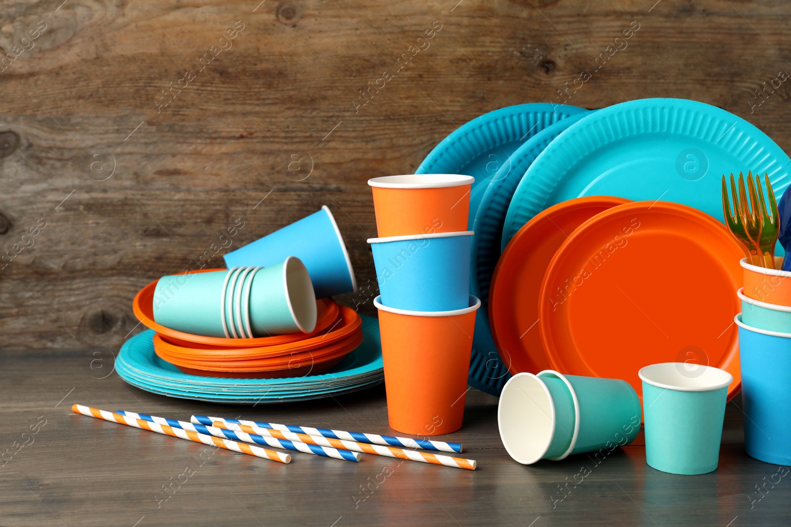 Photo of Set of bright disposable tableware on wooden table