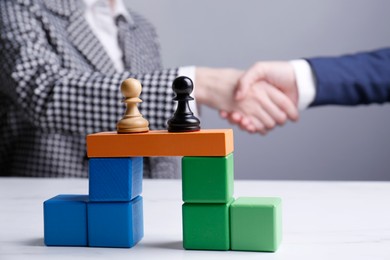 Photo of Businesspeople shaking hands against grey background, focus on bridge made of colorful blocks with pawns. Connection, relationships and deal concept