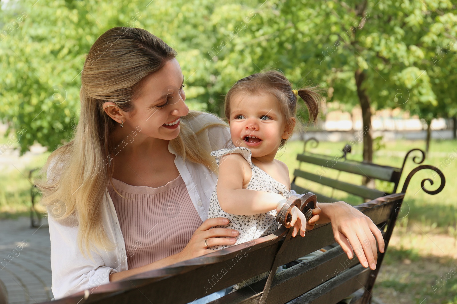 Photo of Happy mother with her daughter sitting on bench in park