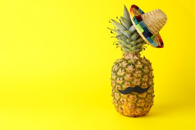 Pineapple with Mexican sombrero hat and fake mustache on yellow background, space for text