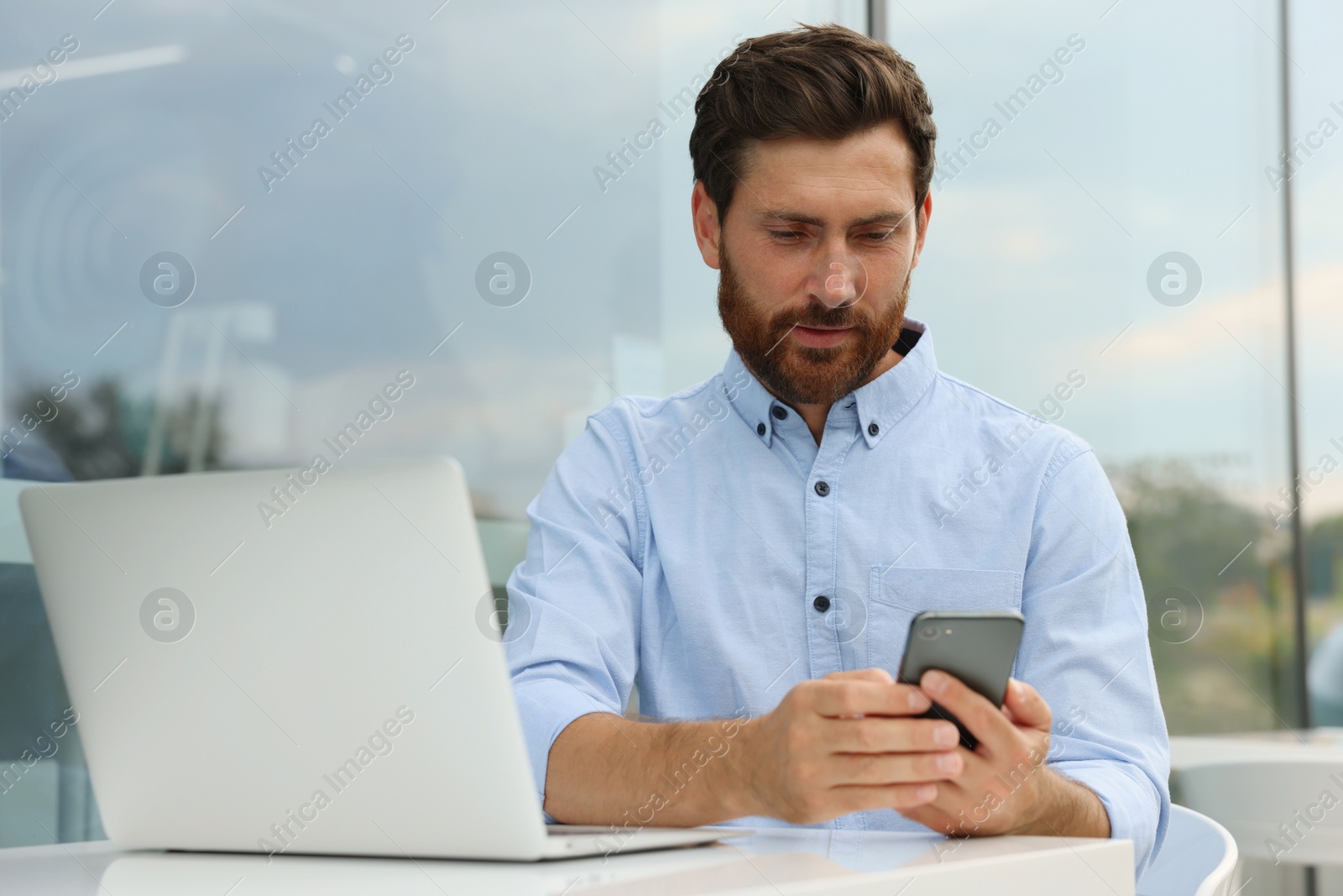 Photo of Handsome man with smartphone and laptop in outdoor cafe