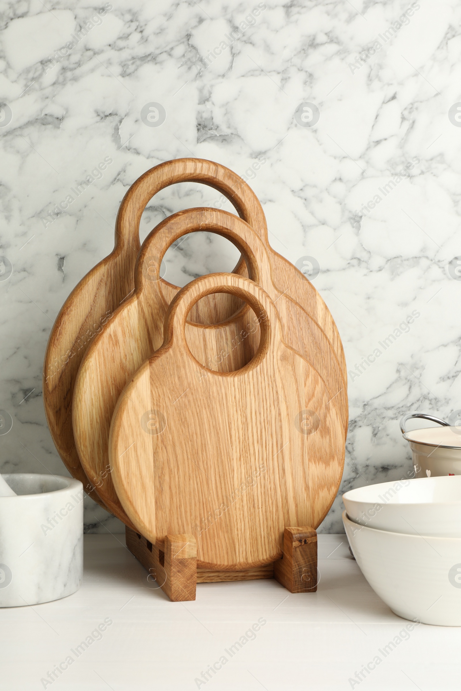 Photo of Wooden cutting boards and bowls on white table near marble wall