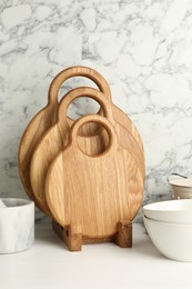 Wooden cutting boards and bowls on white table near marble wall