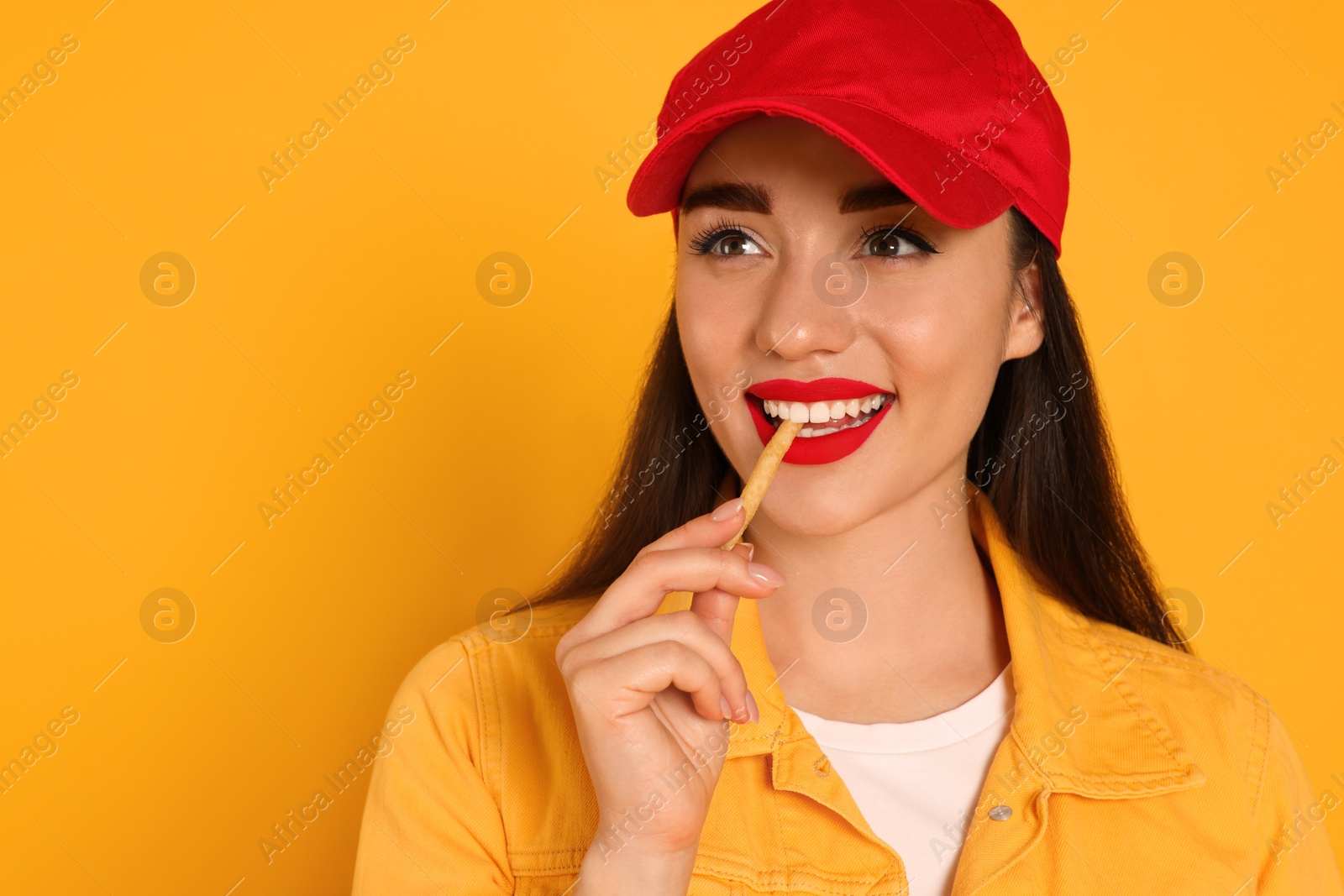 Photo of Beautiful young woman eating French fries on yellow background. Space for text