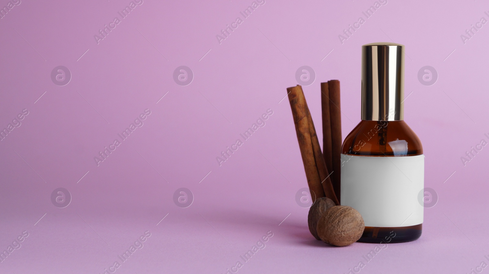 Photo of Bottle of luxurious perfume and spices on light purple background. Space for text